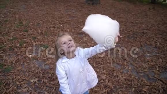金发小女孩正在城市公园吃甜棉花糖美丽的小女孩在吃糖果棉花糖儿童饮食视频的预览图
