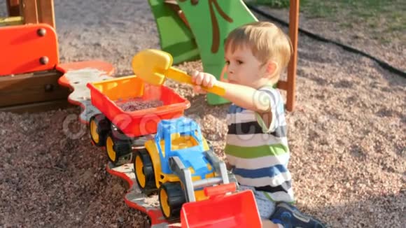 4k视频小男孩在沙箱里玩用塑料铲子在玩具拖车里装砾石和沙子视频的预览图