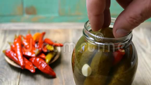 人的手指从木桌上的玻璃罐中取出腌黄瓜或腌黄瓜视频的预览图