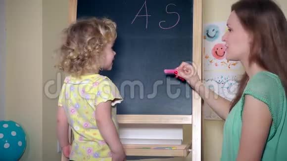 女孩子用粉笔在黑板上画房子和字母视频的预览图