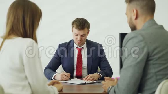 愉快的汽车经销商员工在签署文件后与年轻的买家帅哥握手然后钥匙视频的预览图