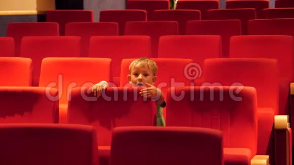 有趣的孩子在空荡荡的电影院大厅里坐在椅子上焦躁不安视频的预览图