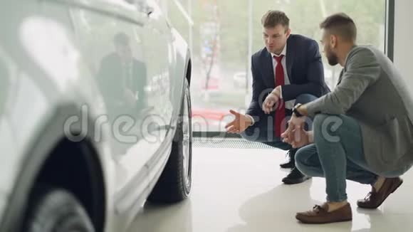 两个男人热情的顾客和友好的推销员正在交谈和手势讨论汽车模型而蹲在附近视频的预览图