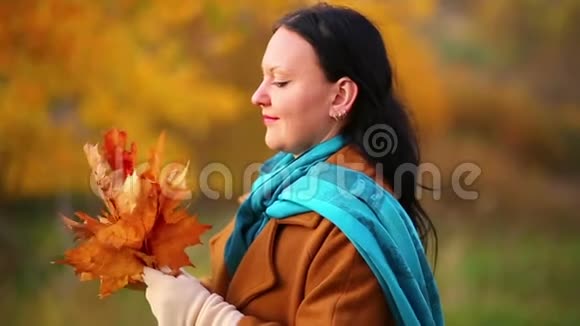 秋天公园里的年轻微笑的女人手里拿着一束枫叶慢动作视频的预览图