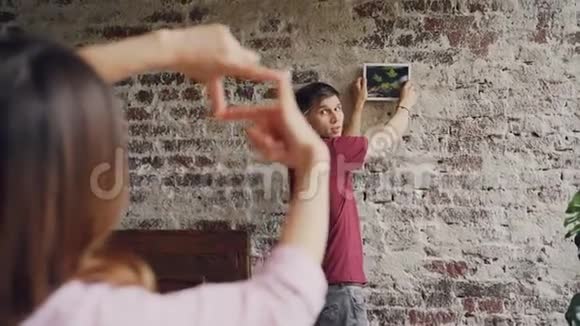 年轻的丈夫选择在砖墙上挂照片而他的妻子正在用她的手指和视频的预览图