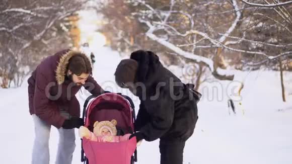 年轻夫妇在冬天和婴儿车里散步年轻的已婚夫妇看着婴儿车而快乐的婴儿视频的预览图