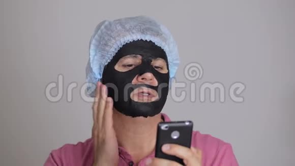 一位45岁的男子脸上戴着一个恢复活力的黑色组织化妆面具打着电话视频的预览图
