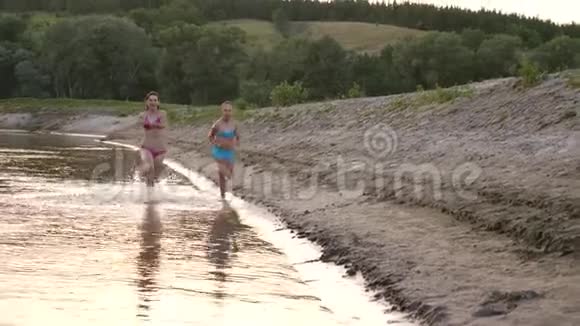 夏天穿着泳衣的年轻女孩沿着海滩跑来跑去笑了起来快乐的孩子们赤脚跑在河岸上视频的预览图