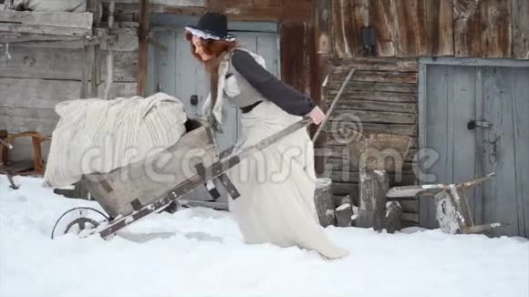 迷人的红发女孩在冬天扛着一辆沉重的手推车勤劳的灰姑娘视频的预览图