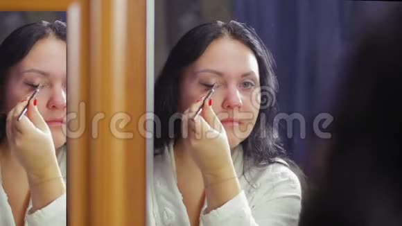 一个穿着白大褂的年轻女子在镜子前用画笔描绘她的眼睛视频的预览图