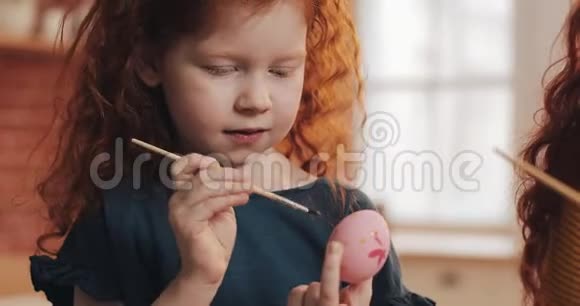 快乐的红头发的小女孩和她的母亲在厨房背景上画复活节彩蛋复活节快乐视频的预览图