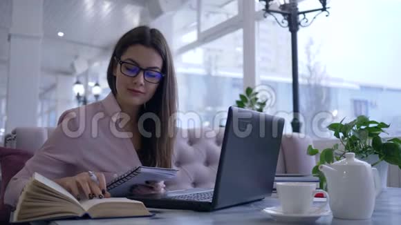 在线教育女学生在笔记本电脑桌上看书和写笔记视频的预览图