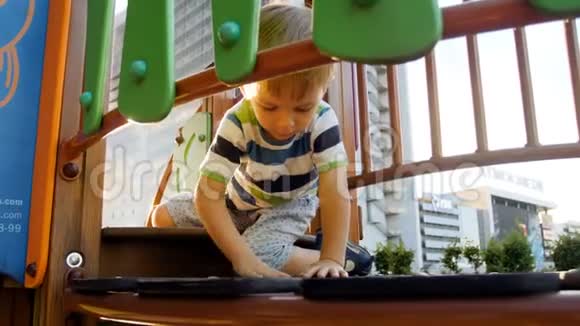 4k镜头可爱的幼儿男孩坐在操场上的木桥上玩耍视频的预览图