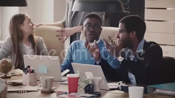 多种族的年轻商人坐在桌子旁合作用笔记本电脑工作在现代健康的办公室交谈视频的预览图
