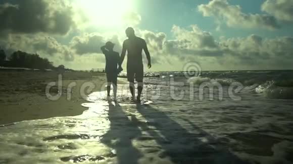 一位年轻的父亲和他的儿子沿着海滨散步阳光灿烂他们在说话家庭幸福信托基金视频的预览图
