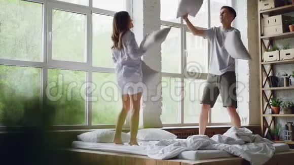 男女朋友在双人床上跳着慢动作打着枕头一起笑着玩视频的预览图