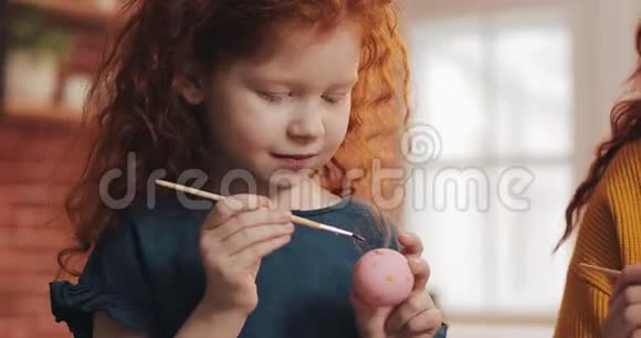 快乐的红头发的小女孩和她的母亲在厨房背景上画复活节彩蛋复活节快乐视频的预览图