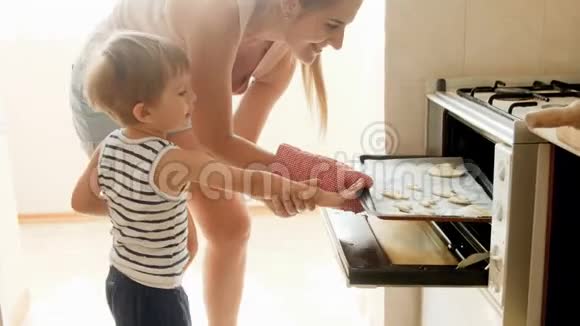 小男孩的4K镜头妈妈把烤盘和饼干放在烤箱里快乐的孩子帮助他妈妈视频的预览图