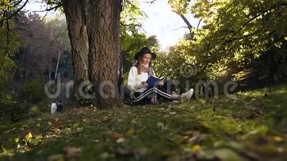 戴着帽子的时髦女孩在公园里放松坐在草地上看书视频的预览图
