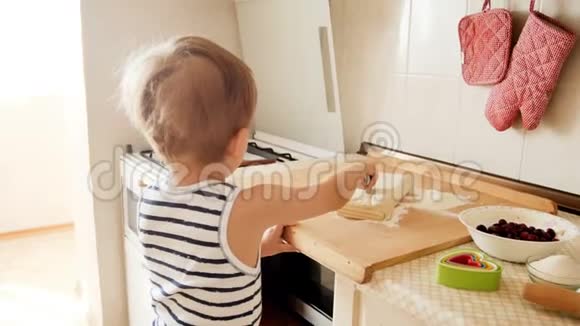 可爱的幼儿男孩用圆刀在木板上切面团的4k镜头视频的预览图