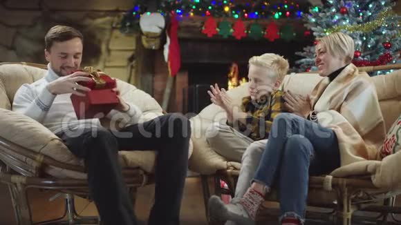 成年男子与妻子和儿子坐在一起看着他的圣诞礼物视频的预览图