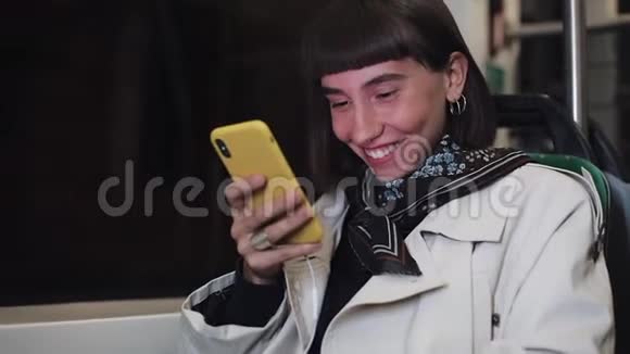 迷人的微笑年轻女子在公共交通工具使用手机她在发短信检查邮件聊天或视频的预览图