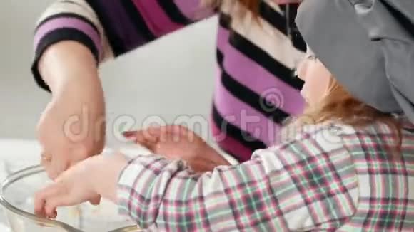 厨师帽子里的小女孩在烹饪室和她妈妈一起混合奶酪视频的预览图