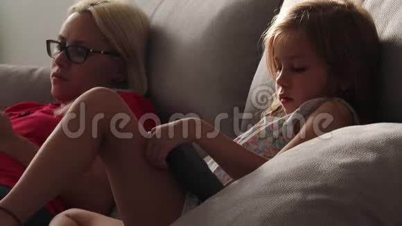 妈妈和女儿坐着看着平板电脑和手机的屏幕视频的预览图