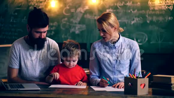父母教一个男孩在学校教室画画教师教一个男孩借鉴绿色学校董事会的背景视频的预览图