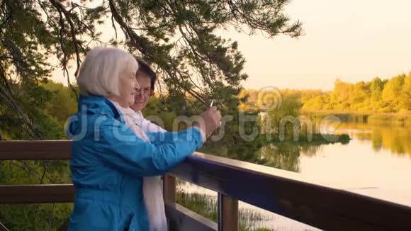两位老妇人在秋景拍摄自拍照片给智能手机视频的预览图