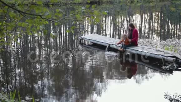 母亲和儿子坐在靠近森林湖的码头上玩耍视频的预览图