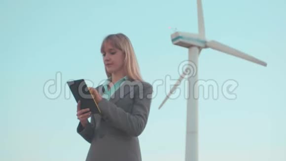 一位成功的女商人站在户外手里拿着一块平板电脑在这种背景下风车是为了保护视频的预览图
