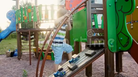 4k视频有趣的蹒跚学步的男孩在公园的儿童操场上攀爬木制订书机视频的预览图
