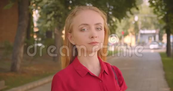 年轻美丽的白种人女性穿着红色的裙子看着站在公园户外的摄像机视频的预览图