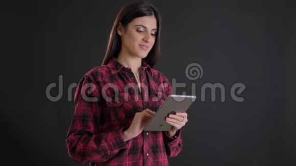 年轻美丽的白种人长发女孩微笑着观看平板电脑的肖像黑色背景视频的预览图