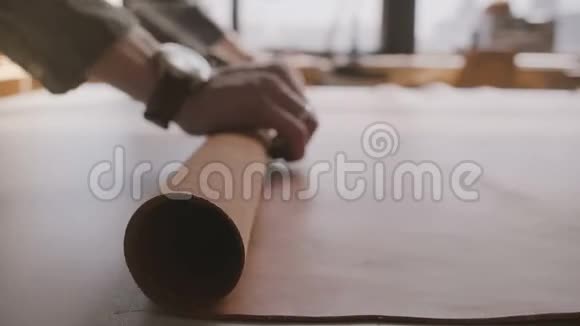 特写镜头的男工艺手滚动一大块宽皮材料在一个卷轴上的制造桌视频的预览图