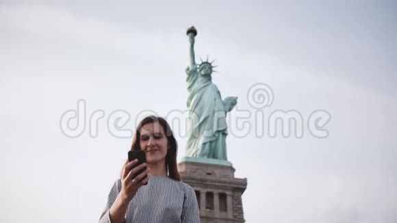快乐美丽微笑的白种人旅游女孩在纽约自由女神像做视频电话慢动作视频的预览图