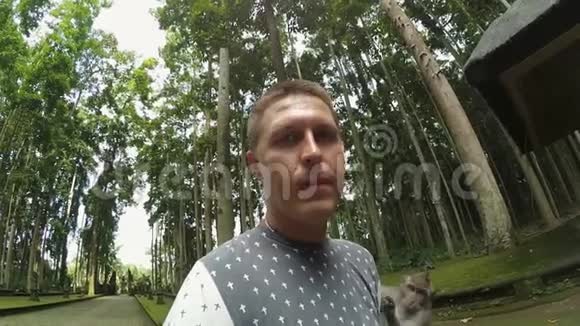 白种人可爱的家伙站在公园里灰色的猴子爬在他的身上视频的预览图