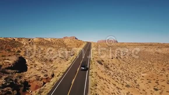 无人机在汽车上方沿着空旷的沙漠道路移动以揭示惊人的山脉天际线在纪念碑谷美国视频的预览图