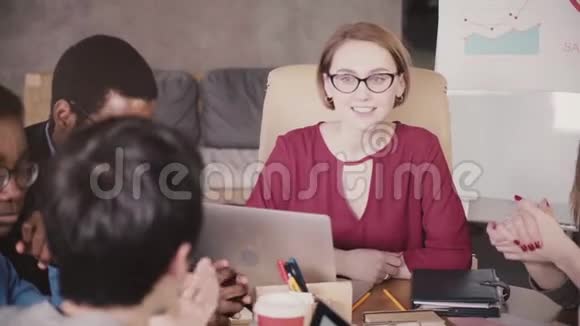 成功的漂亮的欧洲女商人戴着眼镜领导着一个多民族的团队会议在现代办公室的桌子旁视频的预览图