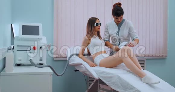 女士腿上的激光脱毛那个女孩躺在治疗室的医疗眼镜里的沙发上这就是视频的预览图