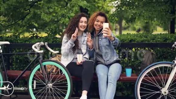 相当粗心的女孩正在自拍智能手机摆姿势拿着咖啡坐在公园里骑自行车视频的预览图