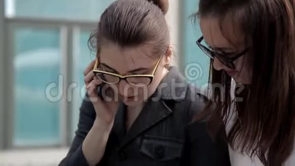 两个年轻的商业女孩坐在商业中心附近的公园里和商人通电话商务视频的预览图