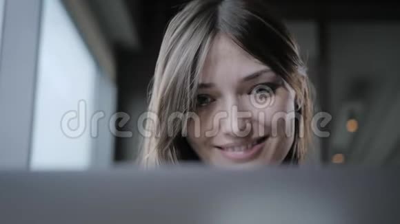 年轻的女人微笑着看着笔记本电脑的屏幕女孩博客浏览互联网聊天在咖啡店里的位置视频的预览图