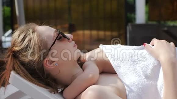 年轻妈妈和小女孩睡在露天游泳池的休息室里视频的预览图