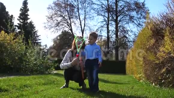 一个年轻的女孩带着一个孩子在草坪上的公园里玩耍女孩做肥皂泡孩子接住A视频的预览图