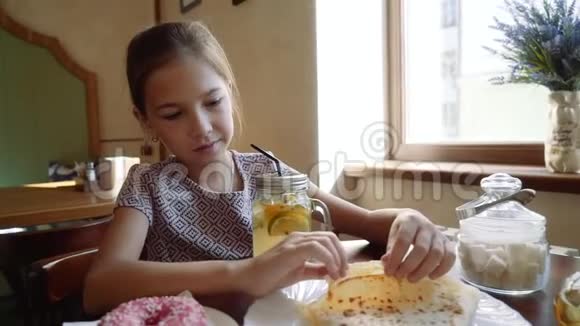 美丽的年轻女孩坐在咖啡馆里用吸管喝鸡尾酒女孩吃煎饼视频的预览图