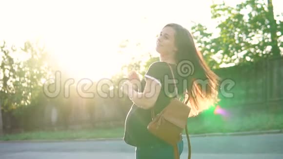 美丽的怀孕女孩穿着T恤和背包在夕阳的照耀下抚摸着她的肚子视频的预览图
