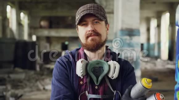 站在废弃建筑内戴着帽子手套和面具的英俊留胡子男子涂鸦艺术家的特写肖像视频的预览图