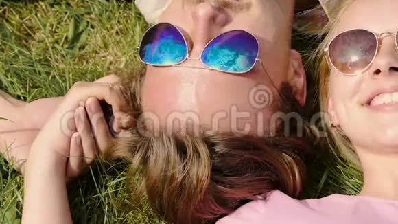 幸福的一对夫妇戴着太阳镜躺在草地上双手捧着天空的倒影视频的预览图